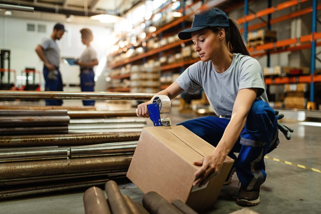 Young woman working in warehouse and taping cardboard box for shipment as she provide packing and unpacking service.